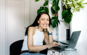 dojrzała kobieta siedząca przy komputerze, wśród kwiatów, opisująca zestaw objawów menopauzy