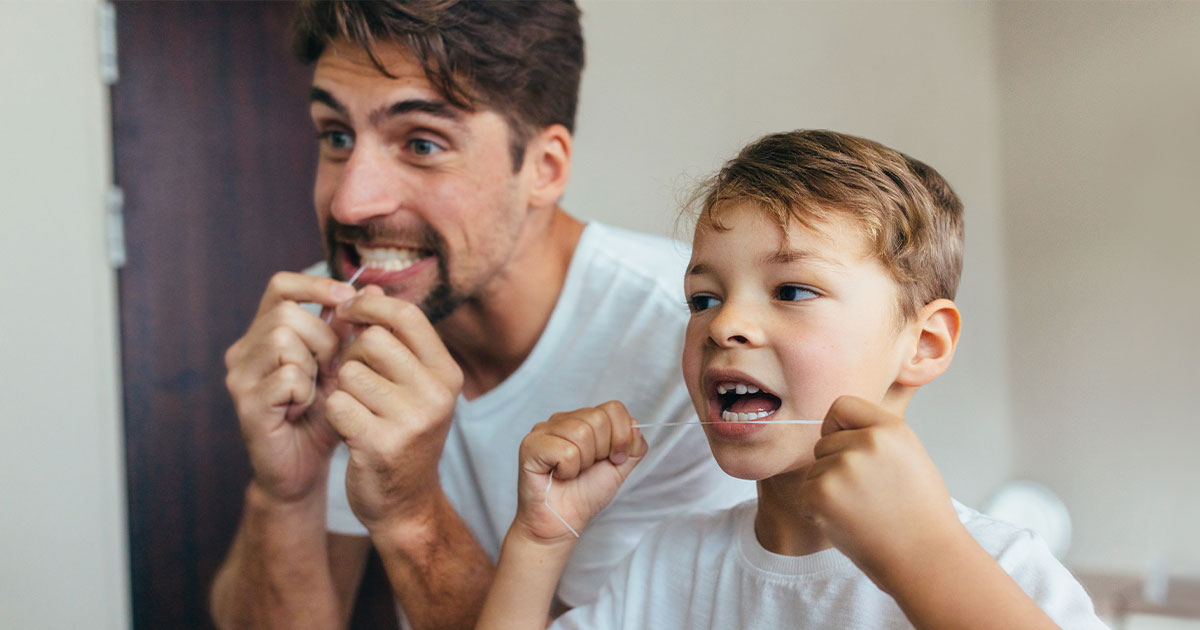 Father and son flossing their teeth in front of a mirror