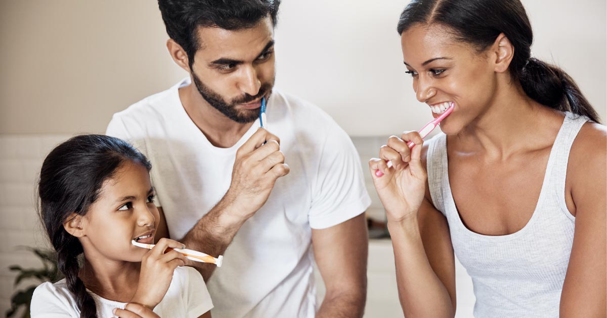 Family of three happily brushing their teeth together