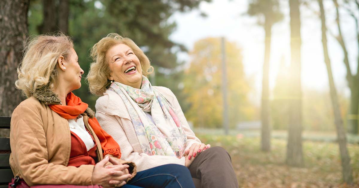 Two older women sitting on a park bench and laughing