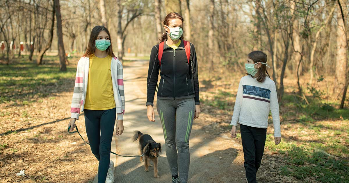 Mother and two daughters wearing medical face masks and hiking with their dog