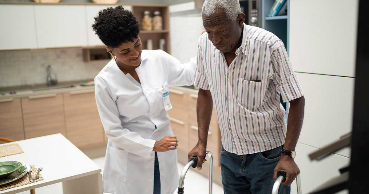 Health care worker helping elderly man use his walker