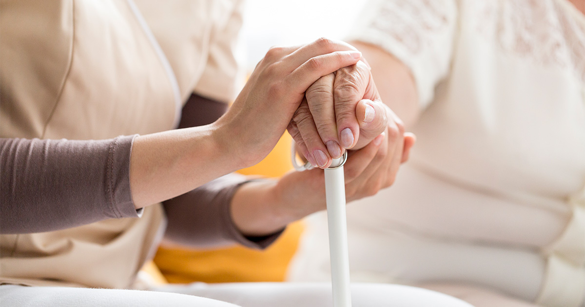 A person holds a white cane, while a health care professional places their hands around theirs.