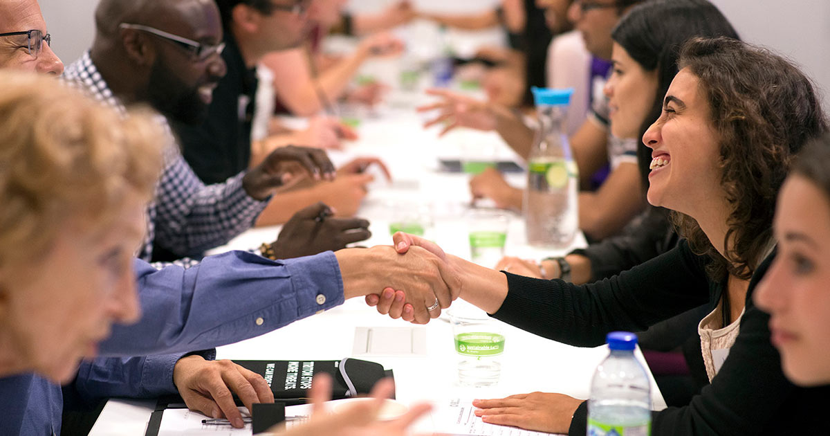 People smiling and shaking hands across a table at a professional event