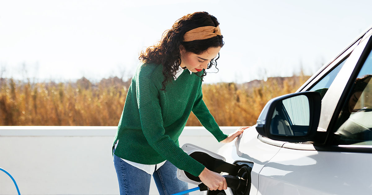 young woman in green sweater topping up EV vehicle