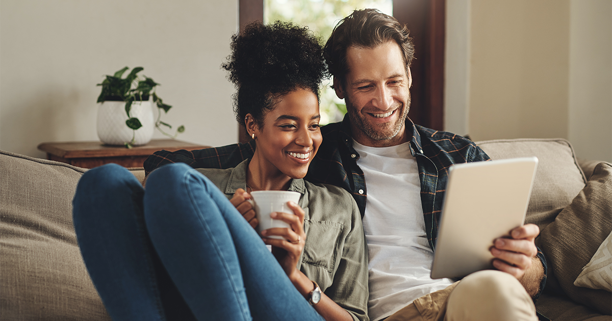 young couple using a digital tablet together while relaxing on a couch at home