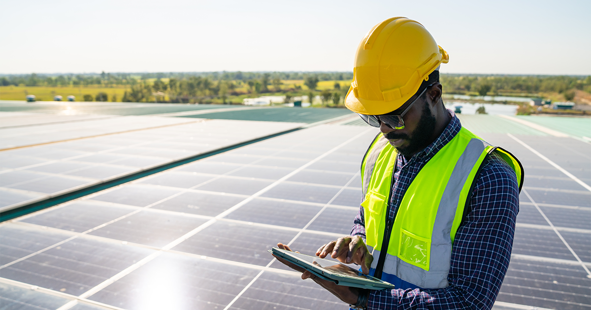 Professional African man engineer using digital tablet maintaining solar cell panels on building rooftop
