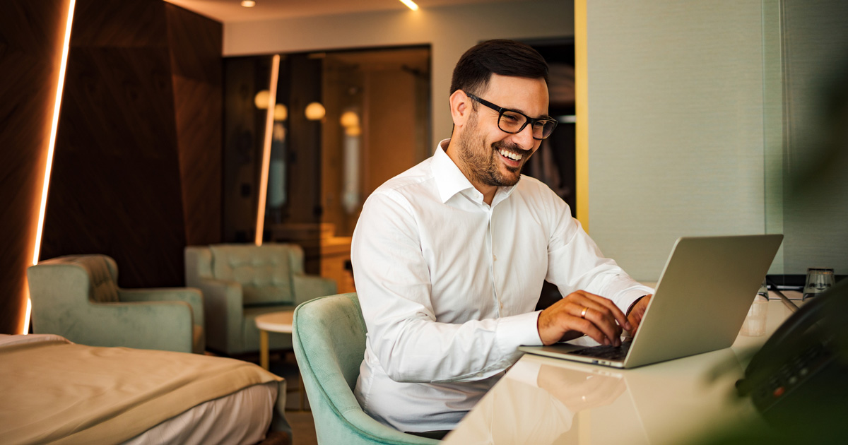 Happy businessman using laptop in the hotel room, portrait
