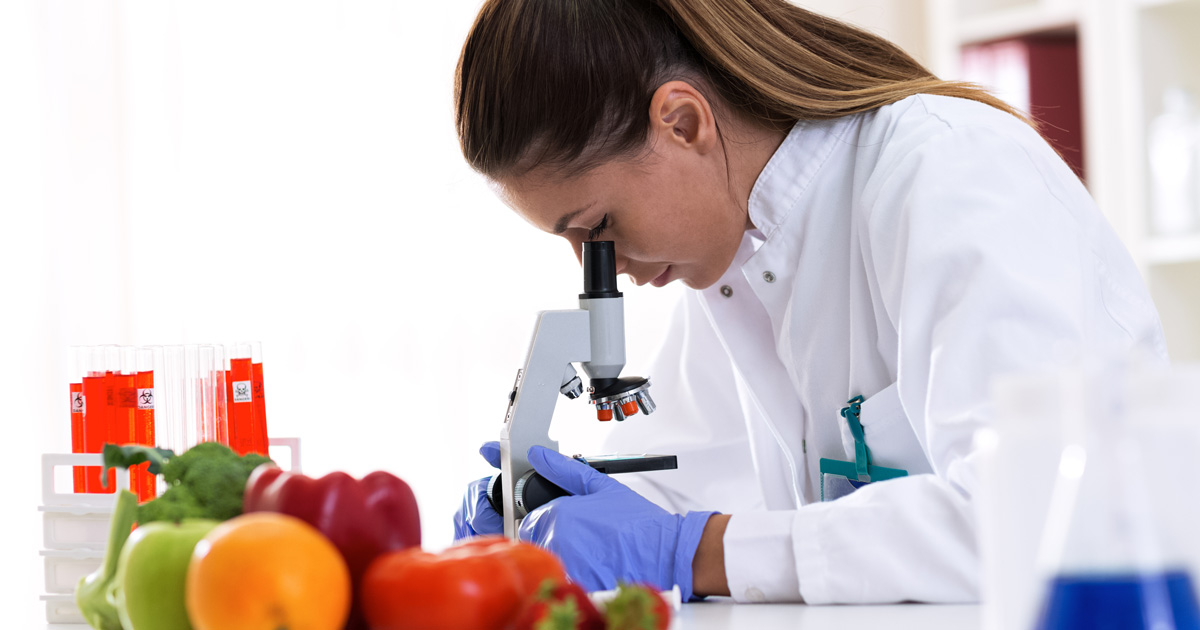 Female scientist in lab coat looks through a microscope