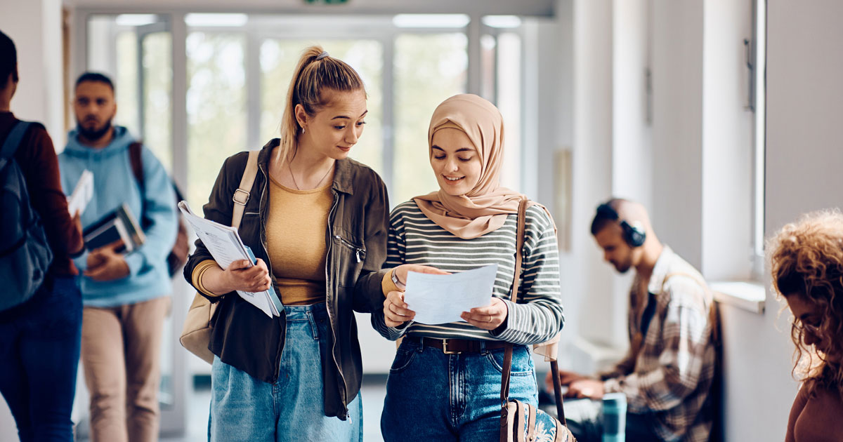 Female students going through lecture notes while walking through the hallway