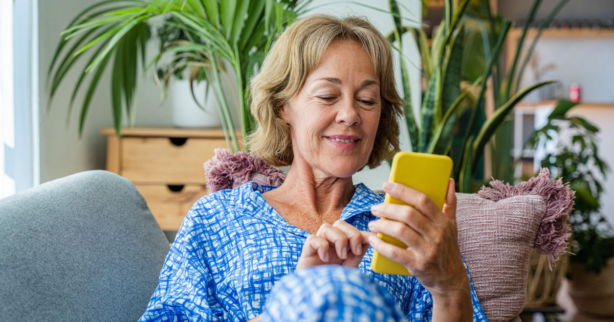50-60 years old pretty female adult relaxing on the sofa and using smartphone