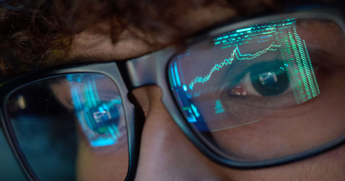 Young business man looking at trading charts reflecting in glasses, close up.