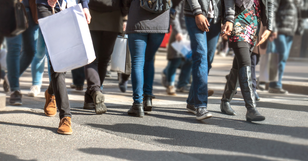 Abstract urban scene of busy city life. The curb is filled with multicultural people crossing while carrying shopping bags. Many punters are buying presents and taking advantage of special discount offers at city retail stores. Shallow focus.