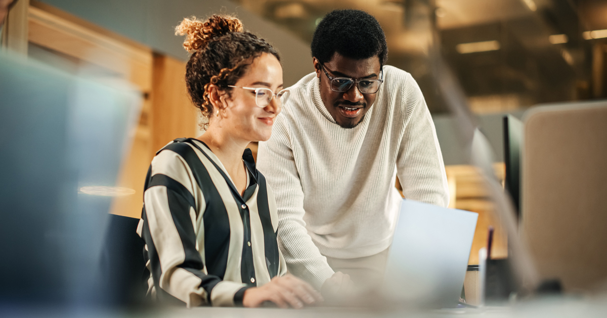 Portrait of Two Creative Colleagues Using Laptop to Discuss Work Project at Office. Young Black Technical Support Specialist Helping Female Customer Relationship Coordinator. Teamwork Concept