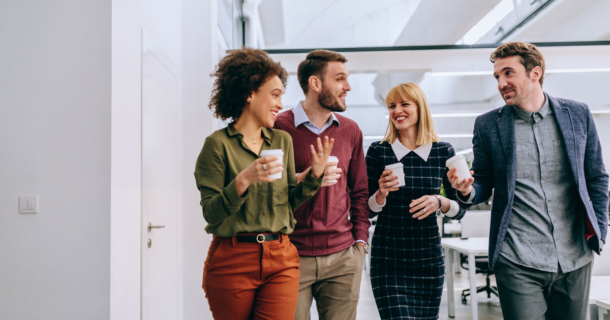 Group of diverse coworkers walking through a corridor in an office, holding paper cups