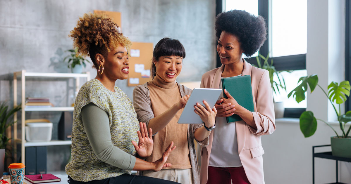 Three young business women talking about project while one holds tablet
