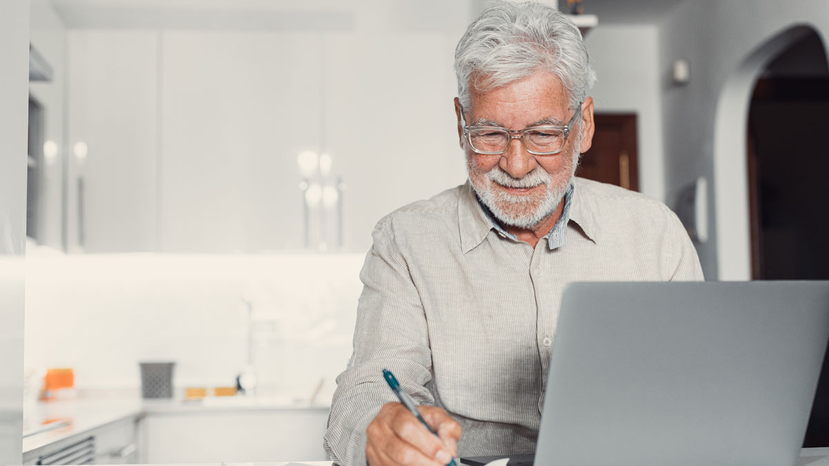Aged remote worker. Concentrated senior male in glasses work on laptop from home office read email electronic document. Old age man employee freelancer sit at kitchen table by pc typing report online