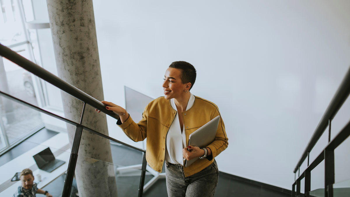 Young short hair business woman walking on office stairs and holding laptop