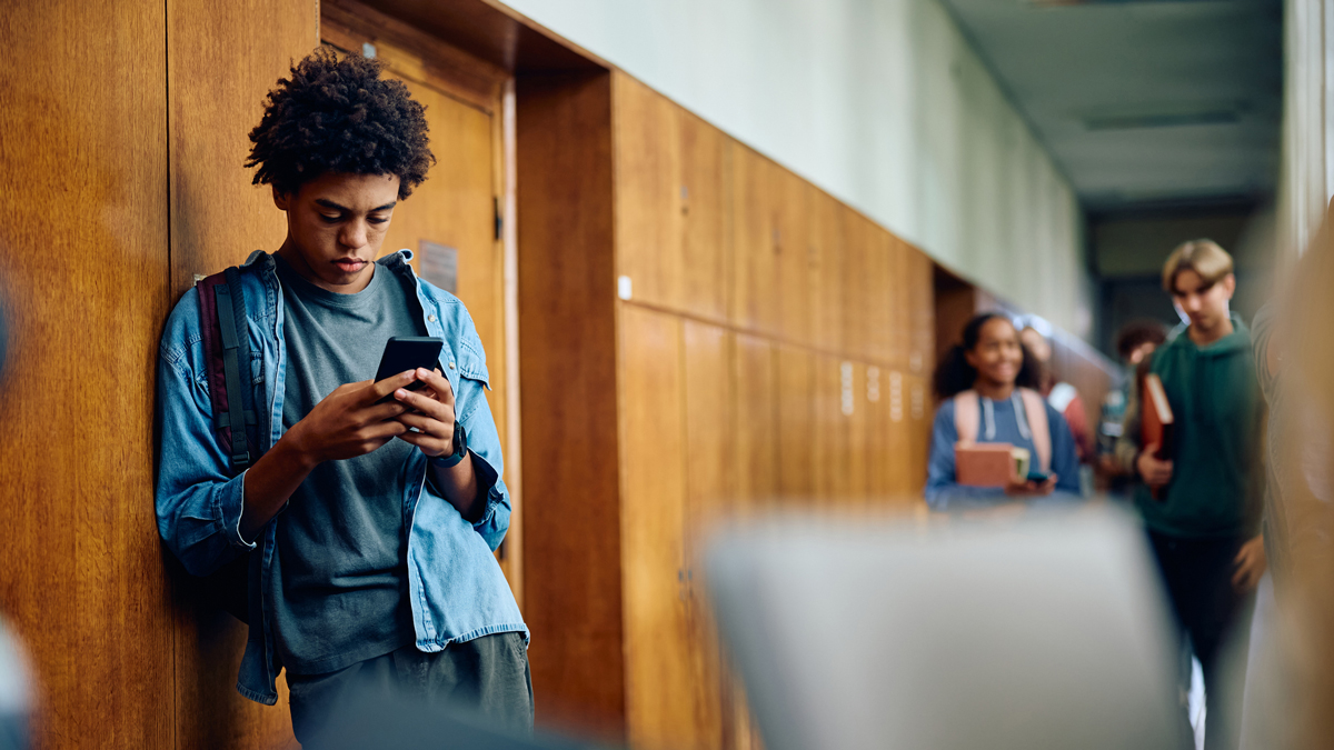 African American high school student using smart phone in a hallway.
