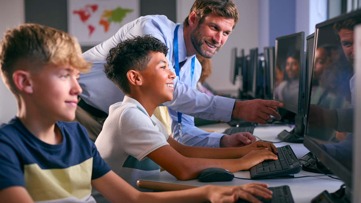 Multi-Cultural Group Of Secondary Or High School Students At Computers In IT Class With Male Teacher