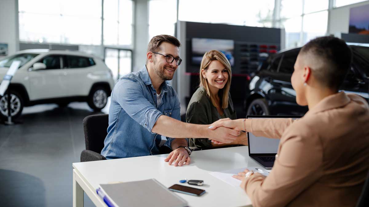 Male customer and female car dealer shaking hands at showroom.