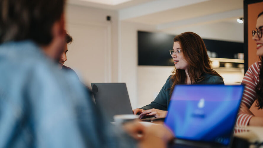 Group of young colleagues engaged in a casual business meeting with laptops at a contemporary office space.