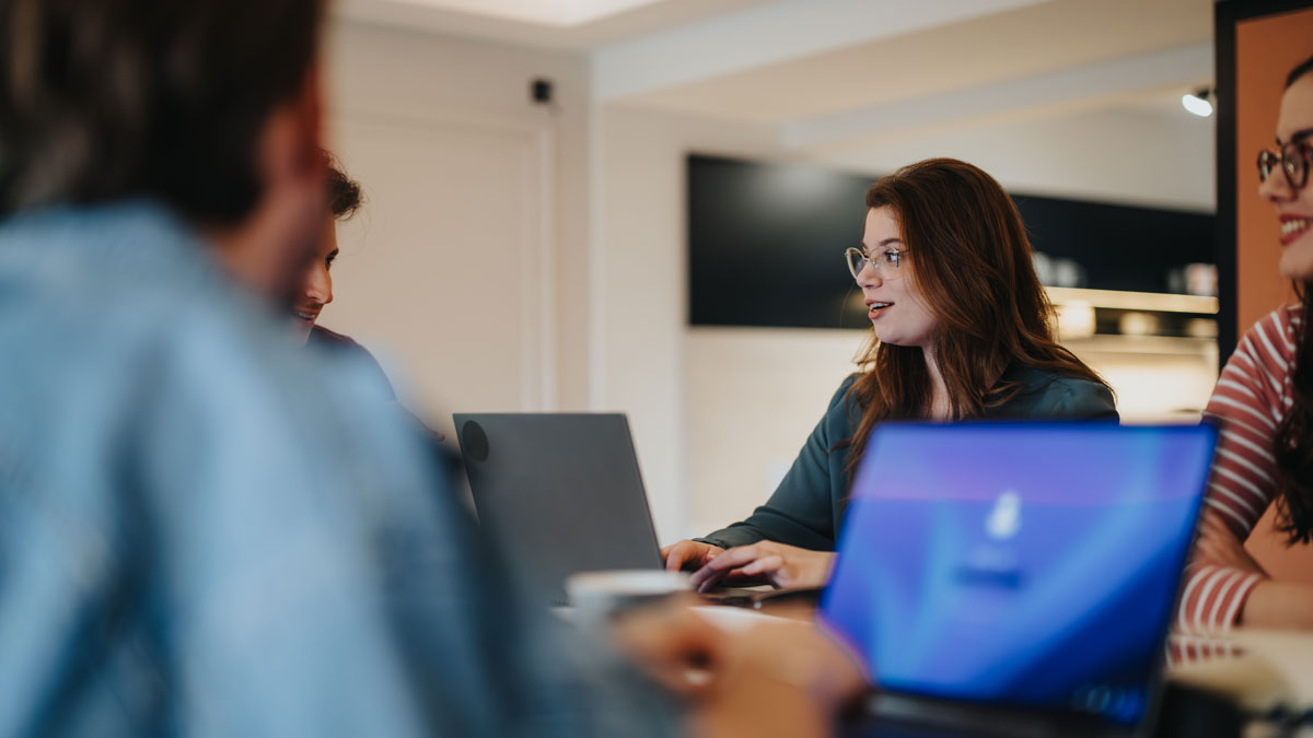 Group of young colleagues engaged in a casual business meeting with laptops at a contemporary office space.