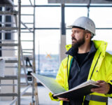 Man engineer standing on construction site, holding blueprints.