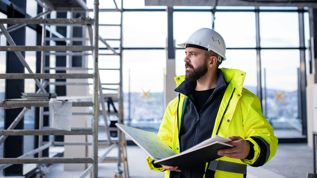 Man engineer standing on construction site, holding blueprints.