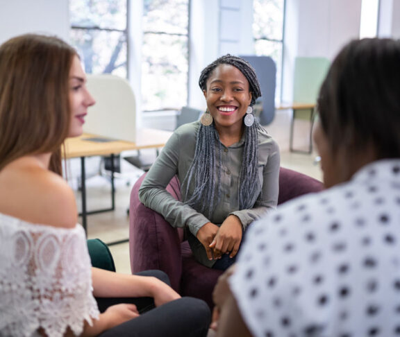 Trendy millennial black african woman sitting on sofa talking woman in a modern co-working space