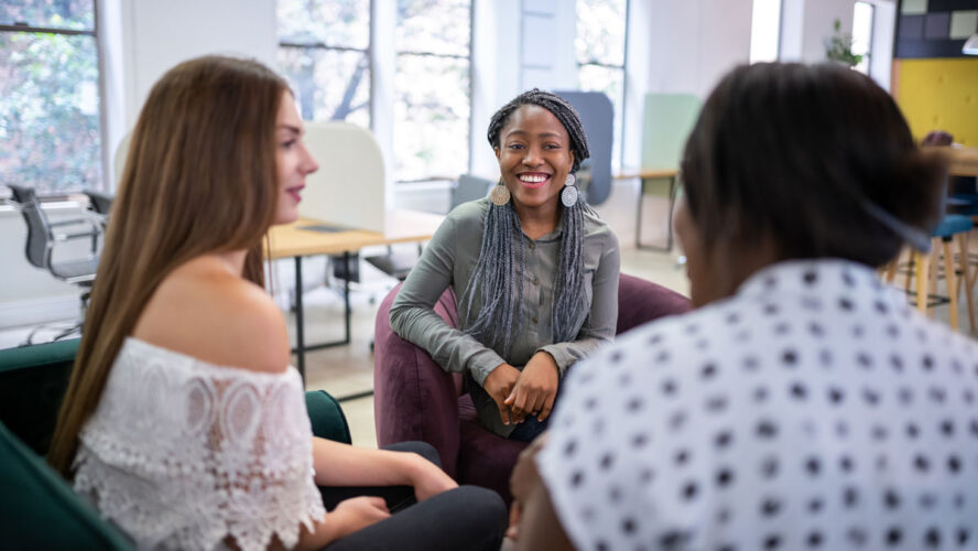 Trendy millennial black african woman sitting on sofa talking woman in a modern co-working space