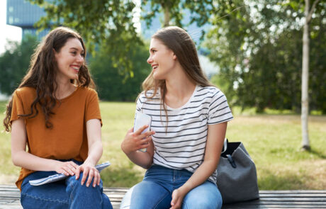Two female caucasian students sitting outside the university campus and chatting
