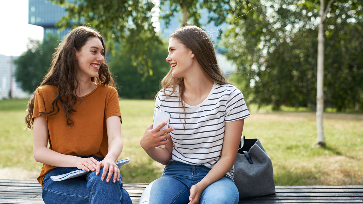 Two female caucasian students sitting outside the university campus and chatting