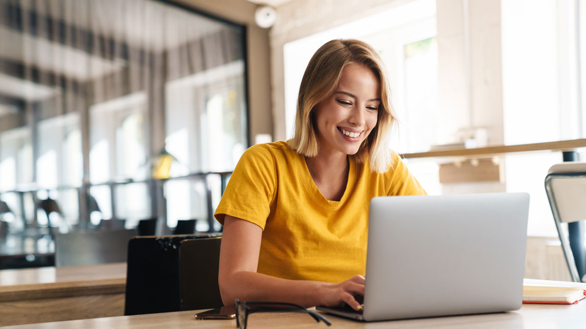 Photo of joyful nice woman using laptop and smiling while sitting