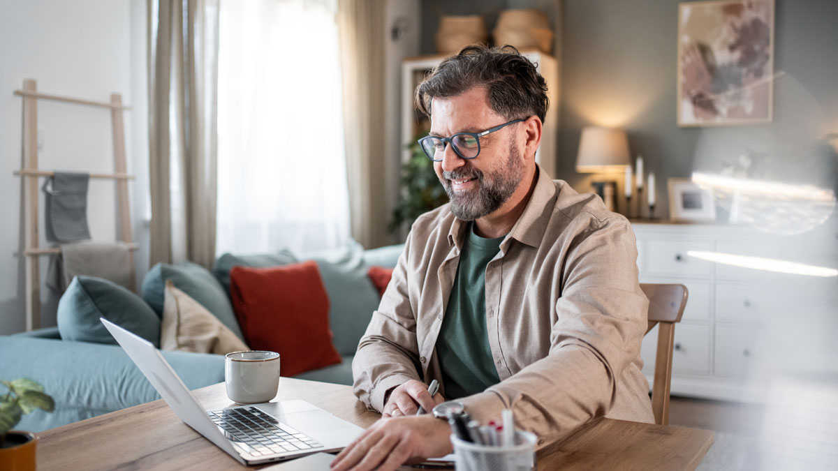 Smiling mature professional working remotely from home office using laptop