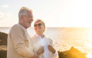 close up and portrait of two happy and active seniors or pensioners having fun and enjoying looking at the sunset smiling with the sea - old people outdoors enjoying vacations together.