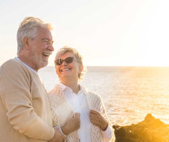 close up and portrait of two happy and active seniors or pensioners having fun and enjoying looking at the sunset smiling with the sea - old people outdoors enjoying vacations together.