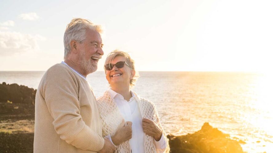 close up and portrait of two happy and active seniors or pensioners having fun and enjoying looking at the sunset smiling with the sea - old people outdoors enjoying vacations together.