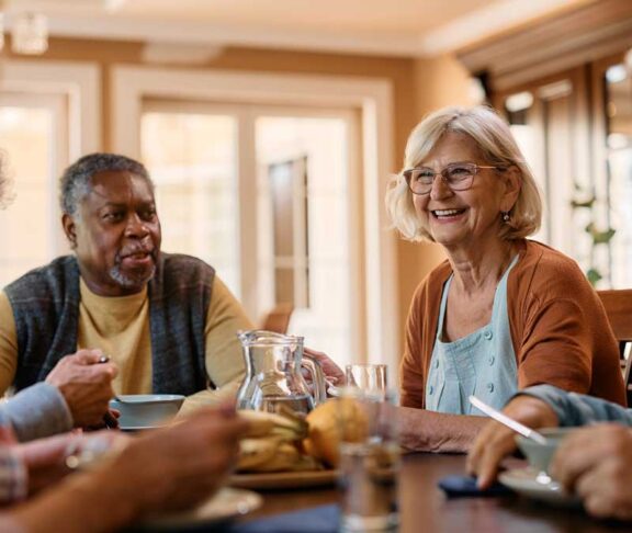 Happy senior woman talks to her friends during lunch in residential care home.