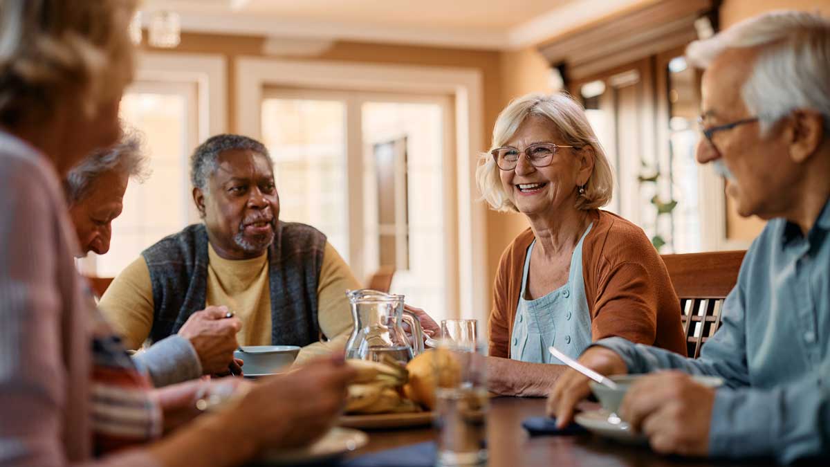 Happy senior woman talks to her friends during lunch in residential care home.