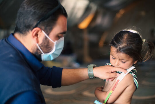 A doctor examines children's malnutrition inside a refugee camp. Malnutrition was measured using a mid-upper arm circumference belt.