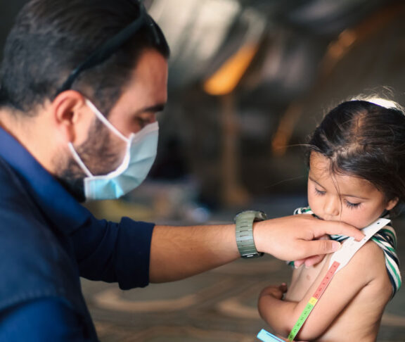 A doctor examines children's malnutrition inside a refugee camp. Malnutrition was measured using a mid-upper arm circumference belt.