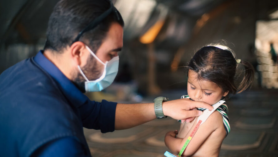 A doctor examines children's malnutrition inside a refugee camp. Malnutrition was measured using a mid-upper arm circumference belt.