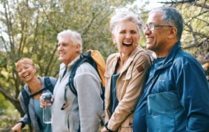 Nature, hiking and happy senior friends bonding, talking and laughing at comic joke in forest. Happiness, fun and group of elderly people trekking together for health, wellness and exercise in woods