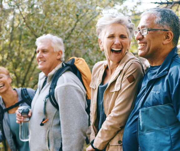 Nature, hiking and happy senior friends bonding, talking and laughing at comic joke in forest. Happiness, fun and group of elderly people trekking together for health, wellness and exercise in woods
