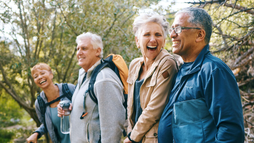 Nature, hiking and happy senior friends bonding, talking and laughing at comic joke in forest. Happiness, fun and group of elderly people trekking together for health, wellness and exercise in woods