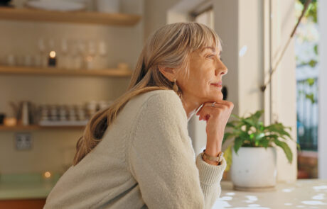 Window, smile and elderly woman with thinking at home for retirement, satisfaction and peace on weekend. Relax, senior person and calm with idea for reflection, mindfulness and good memory in house