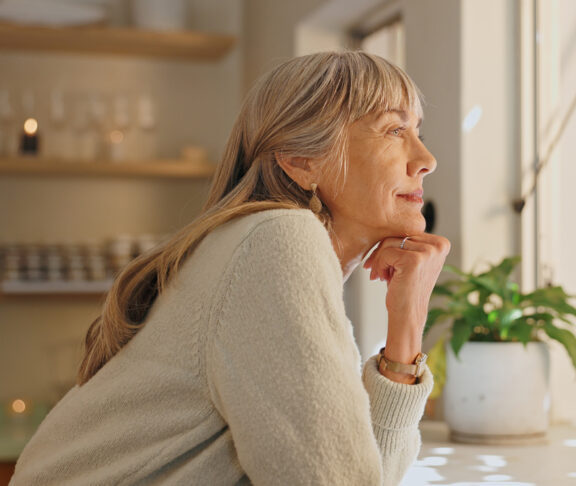 Window, smile and elderly woman with thinking at home for retirement, satisfaction and peace on weekend. Relax, senior person and calm with idea for reflection, mindfulness and good memory in house