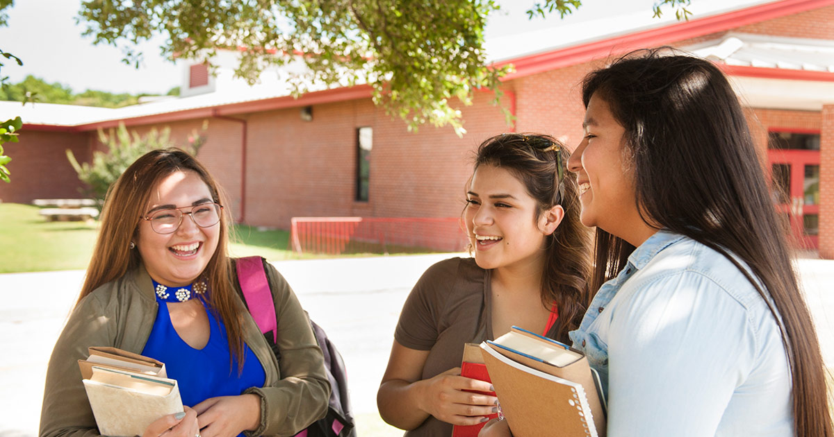 Three Indigenous youths outside a school, laughing