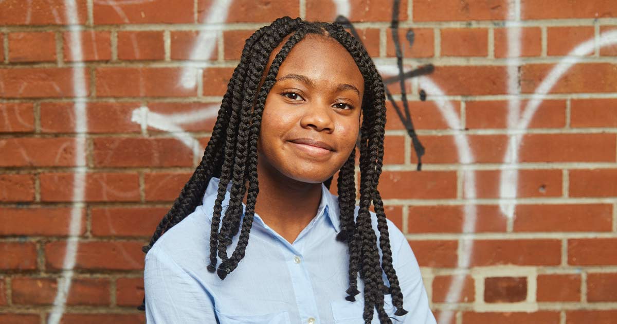 Young female Black mentee smiling in front of a brick wall